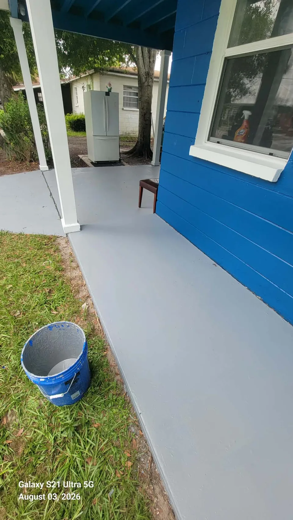 Gray concrete stain on a porch and walkway beside a blue painted home in Brevard County, FL