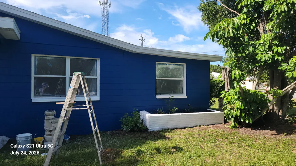 Exterior house painting in progress with ladder and blue siding in Brevard County, FL