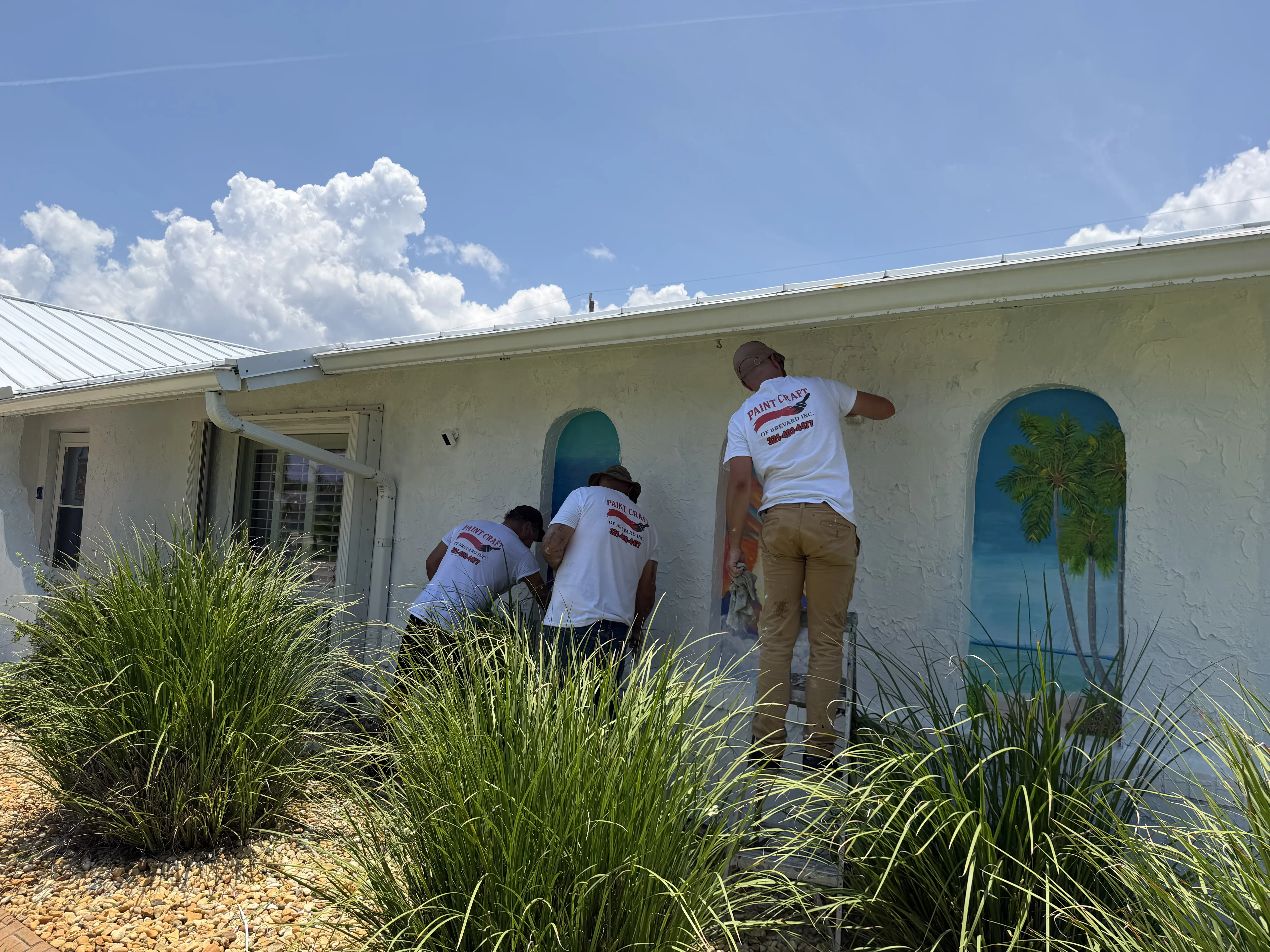 Paint Craft of Brevard crew painting a home exterior with a palm tree mural in Brevard County, FL